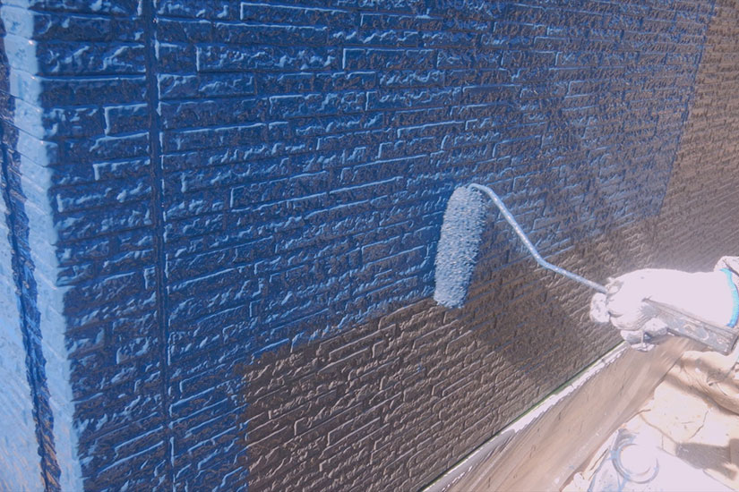 ローラーで青い塗料を外壁に塗っている作業の様子