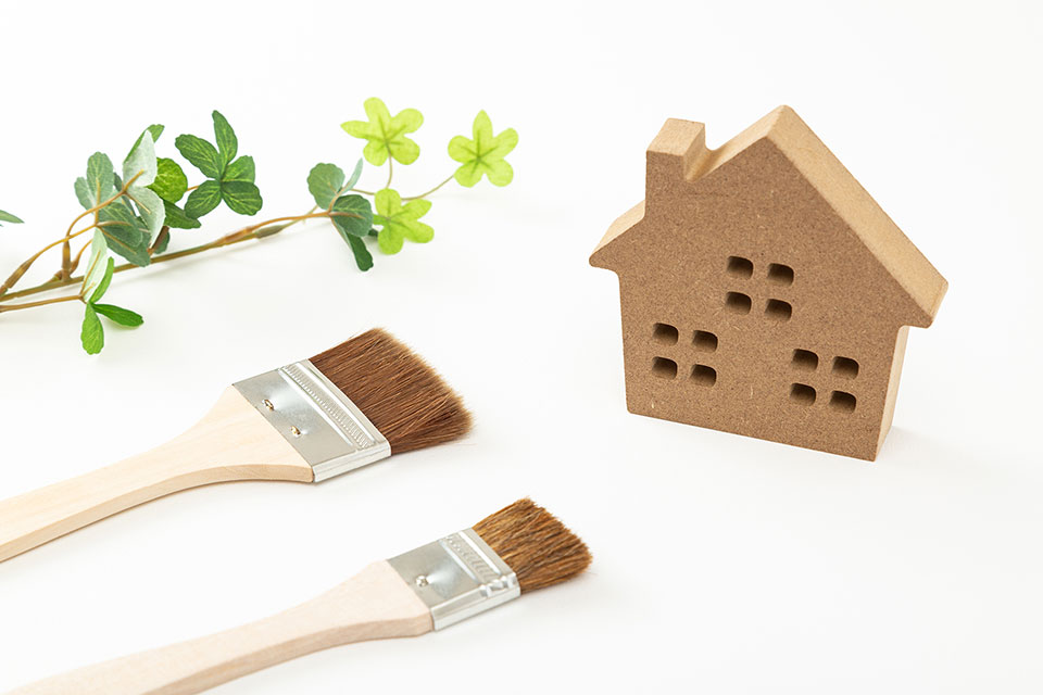 住宅の塗り替えをイメージした、家のミニチュアとブラシが2本置かれた写真