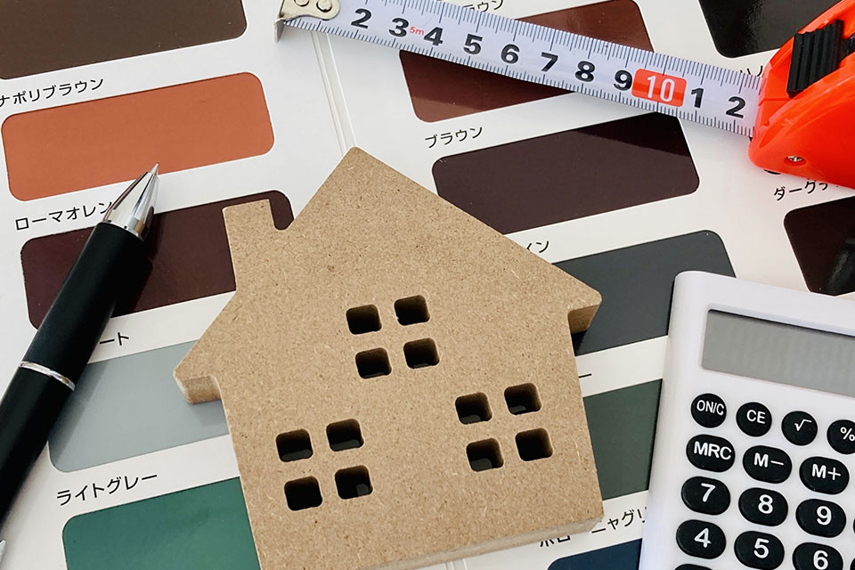 色見本の上に、家のモチーフやボールペン、電卓、メジャーなどが置かれている