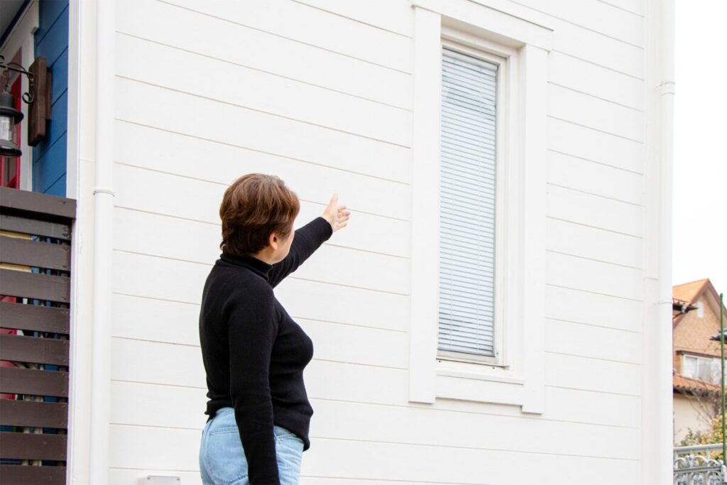 白い外壁の前で、H様が窓の方を指し示している様子。