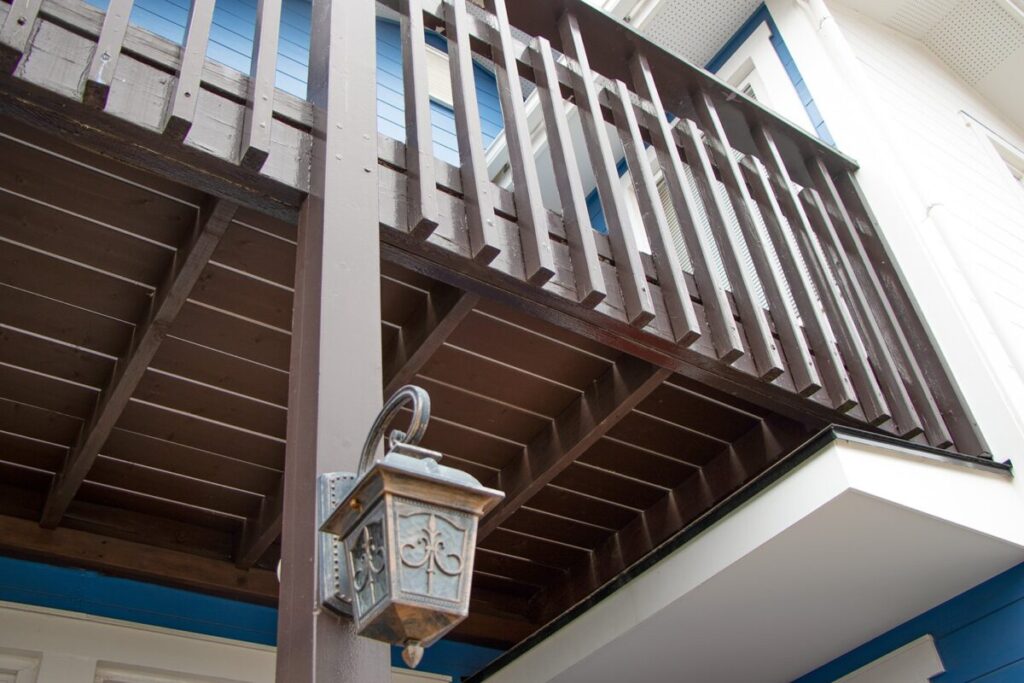 北欧住宅の木製バルコニーを下から見上げた様子。柱や手すりの構造と、装飾的な外灯が取り付けられている。
