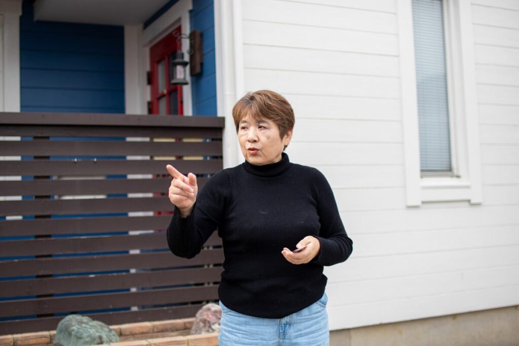 家の前で、H様が手で方向を指し示しながら説明している様子。