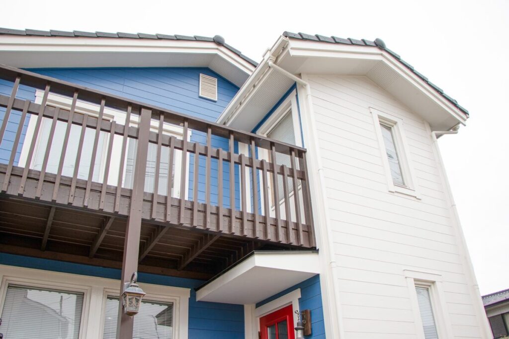 北欧の住宅の外観を見上げた構図。2階の木製バルコニーと赤い玄関ドア、窓や屋根のディテールが見える。